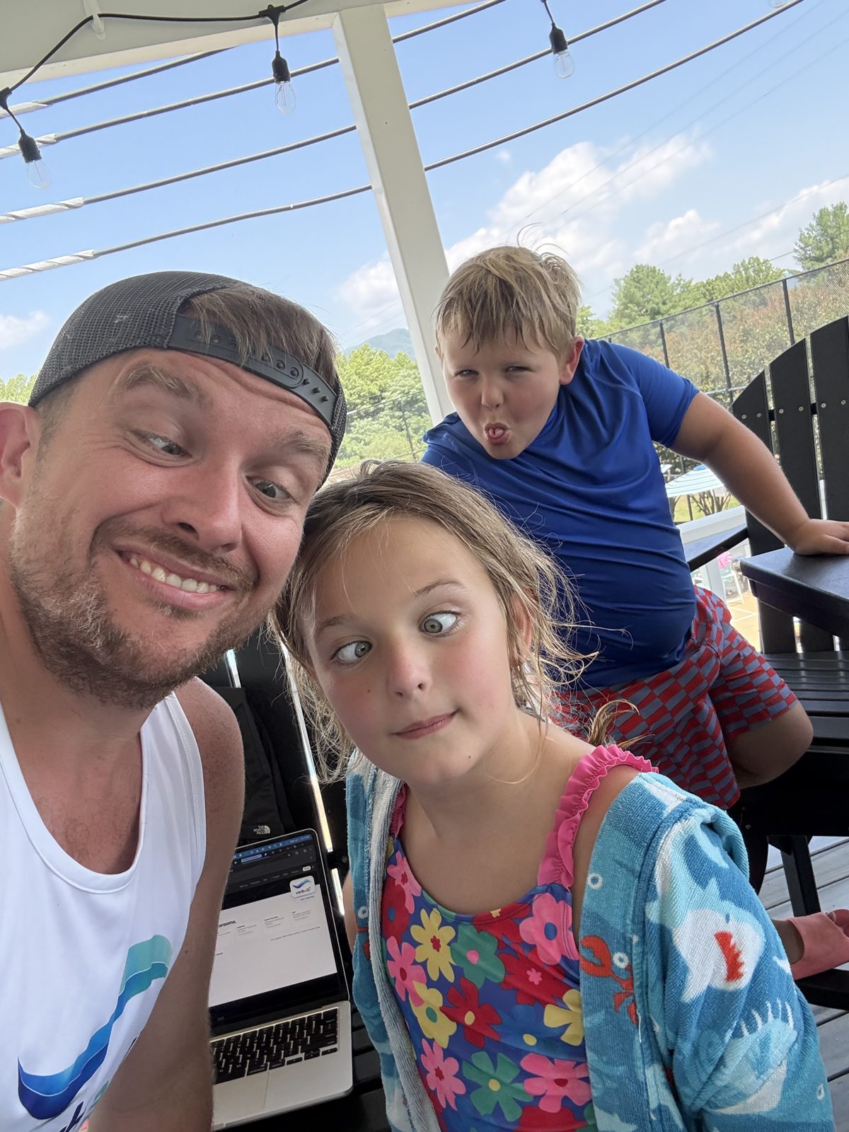 Working on a laptop on the porch with two kids pulling faces